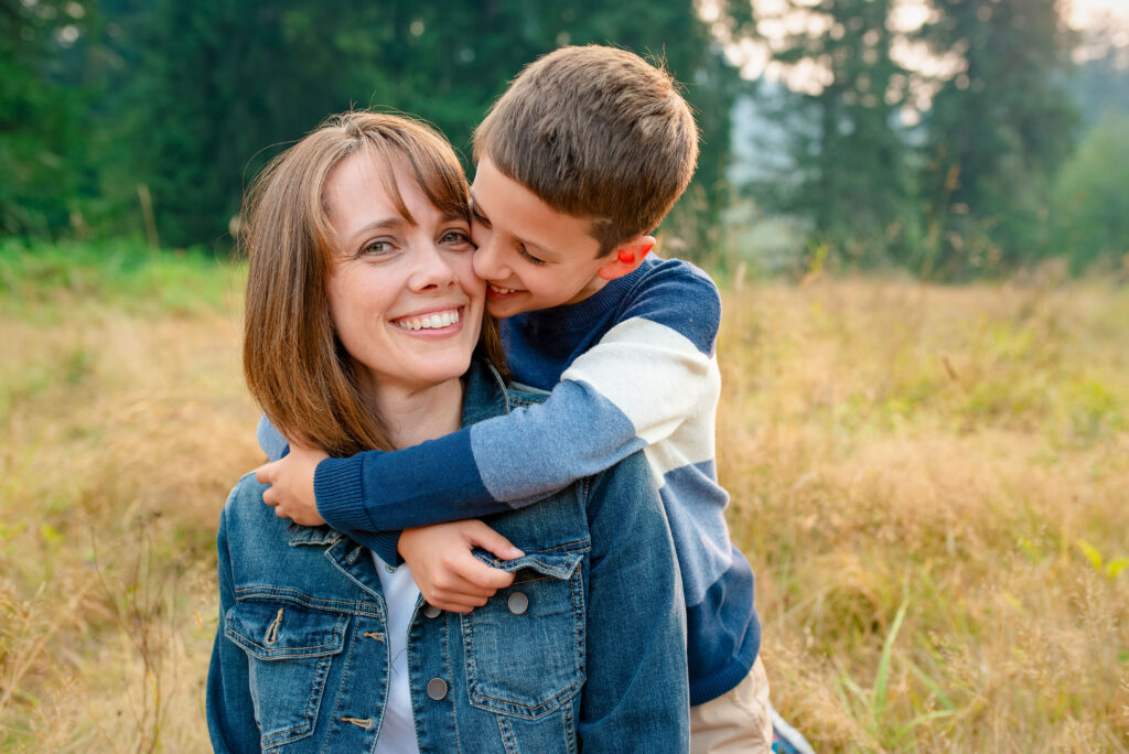Boy hugging his mother in a field at Evans Creek Preserve in Sammamish, WA. Mom is looking at the camera and smiling.