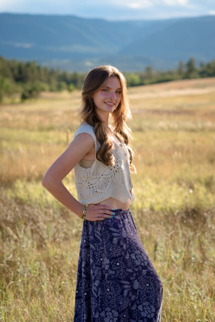 High school senior posing in golden field during a senior session with mountain views and warm natural light