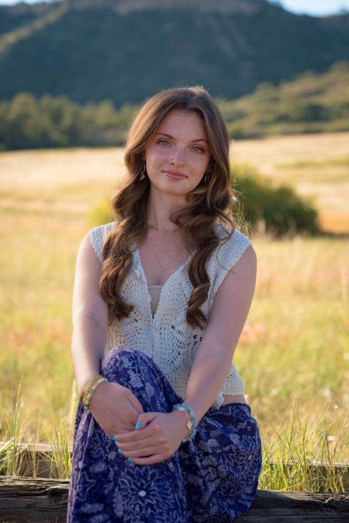 High school senior sitting in tall grass during a Dawson Butte Senior Session with mountain views and warm golden light