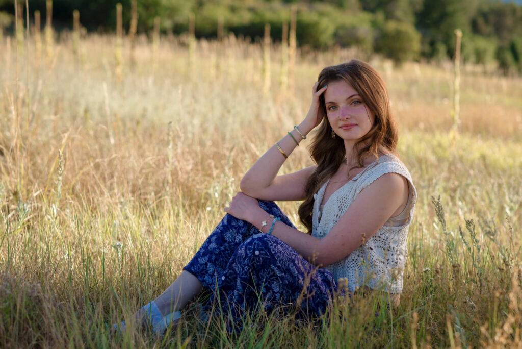 Dawson Butte Senior Session portrait of high school senior sitting in tall grass with warm sunset light in Castle Rock Colorado