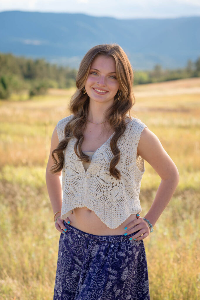 Relaxed senior sitting in golden grass during a Dawson Butte Senior Session with soft sunlight and peaceful mountain scenery