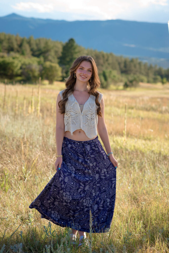 Full-length portrait of high school senior in flowing skirt during a Dawson Butte Senior Session with golden field and mountain views