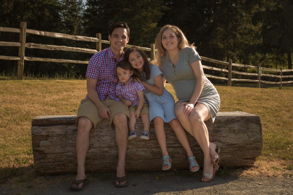 Family sitting on a rustic log smiling during a Denver spring family photo session with a natural Colorado backdrop