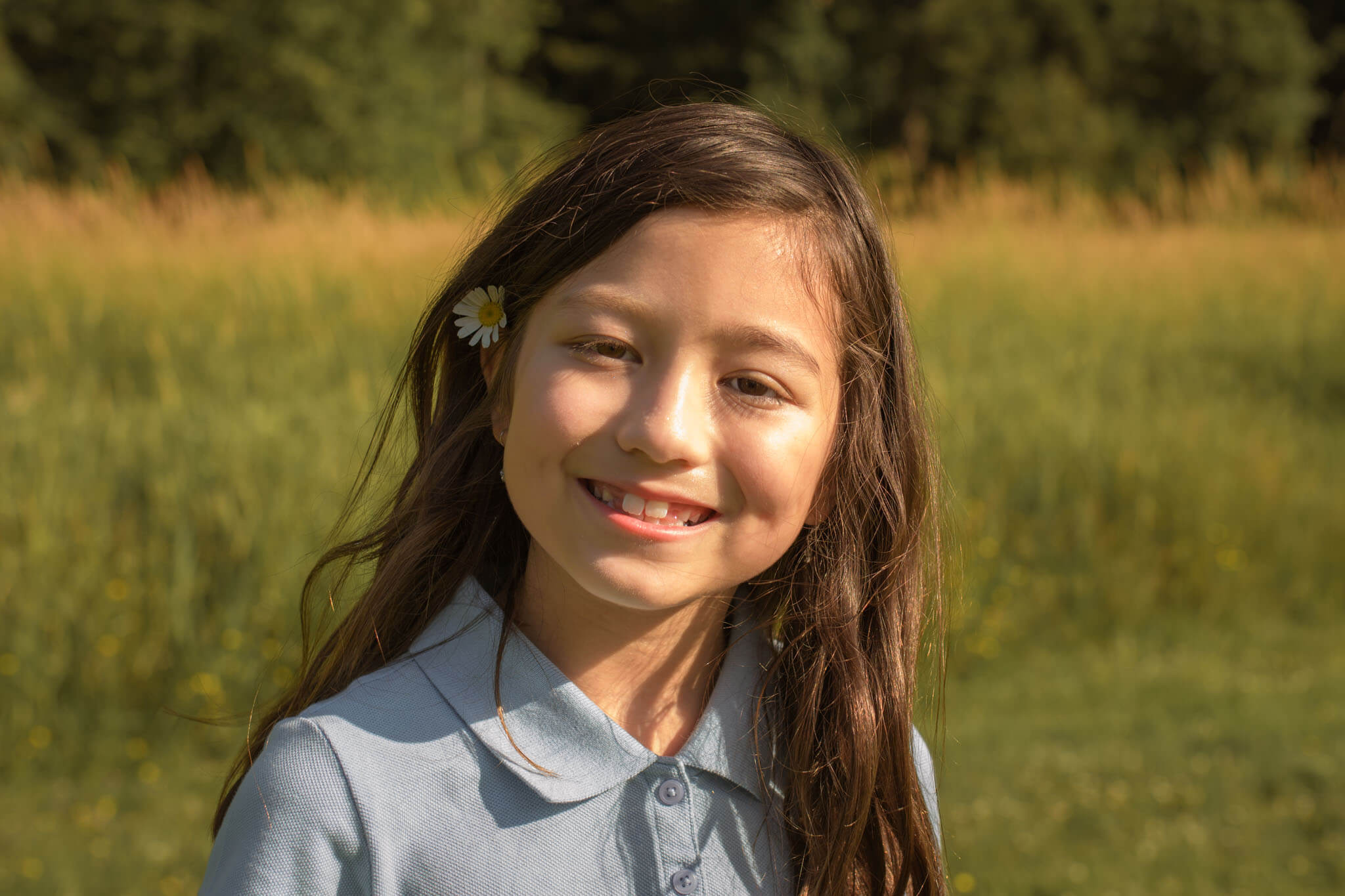 Young girl smiling with a flower in her hair during a Denver spring family photo session in a sunlit field