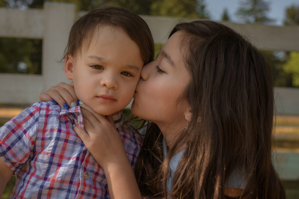 Big sister kissing her little brother on the cheek during a Denver spring family photo session capturing a candid moment