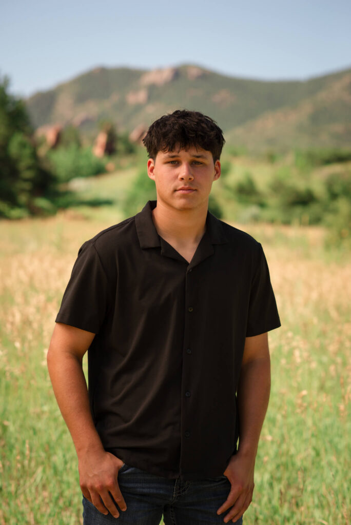 High school senior boy standing in a grassy Colorado field with mountain views during an outdoor Denver senior photo session.