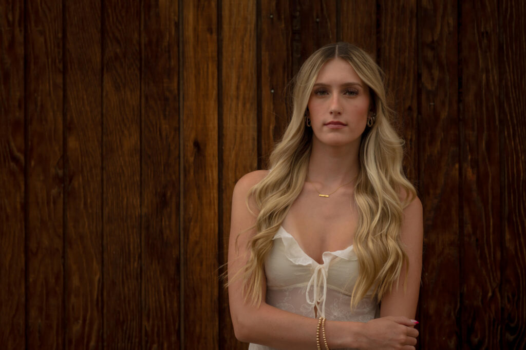 Blonde high school senior girl posing in front of a rustic wood wall during an urban Denver senior photo session.