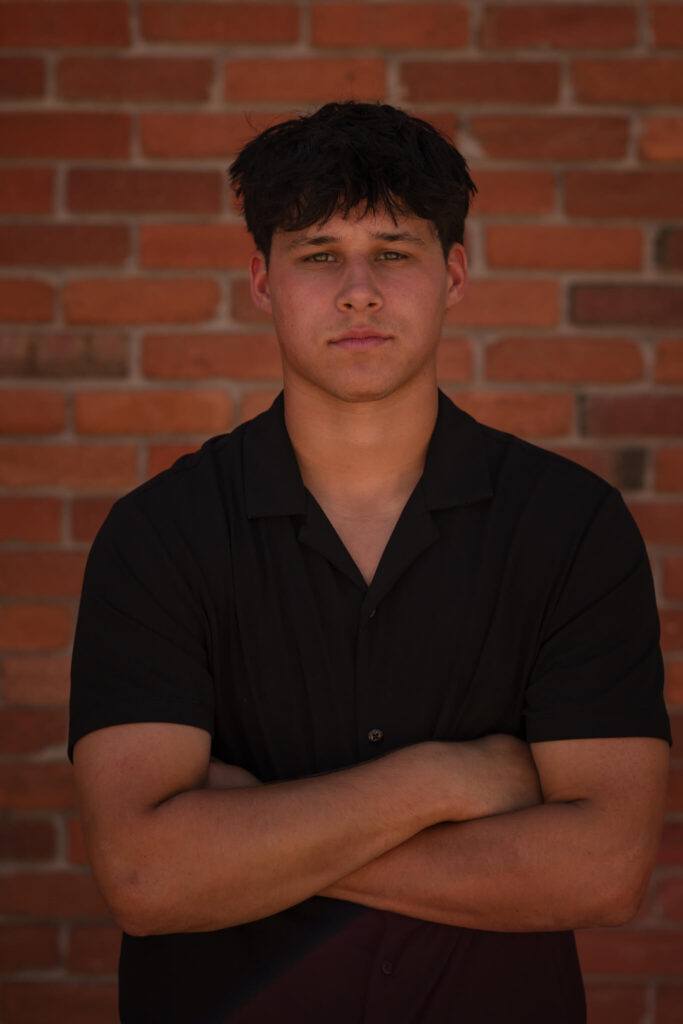 High school senior guy posing in front of a brick wall during an urban Denver senior photo session with a modern city vibe.