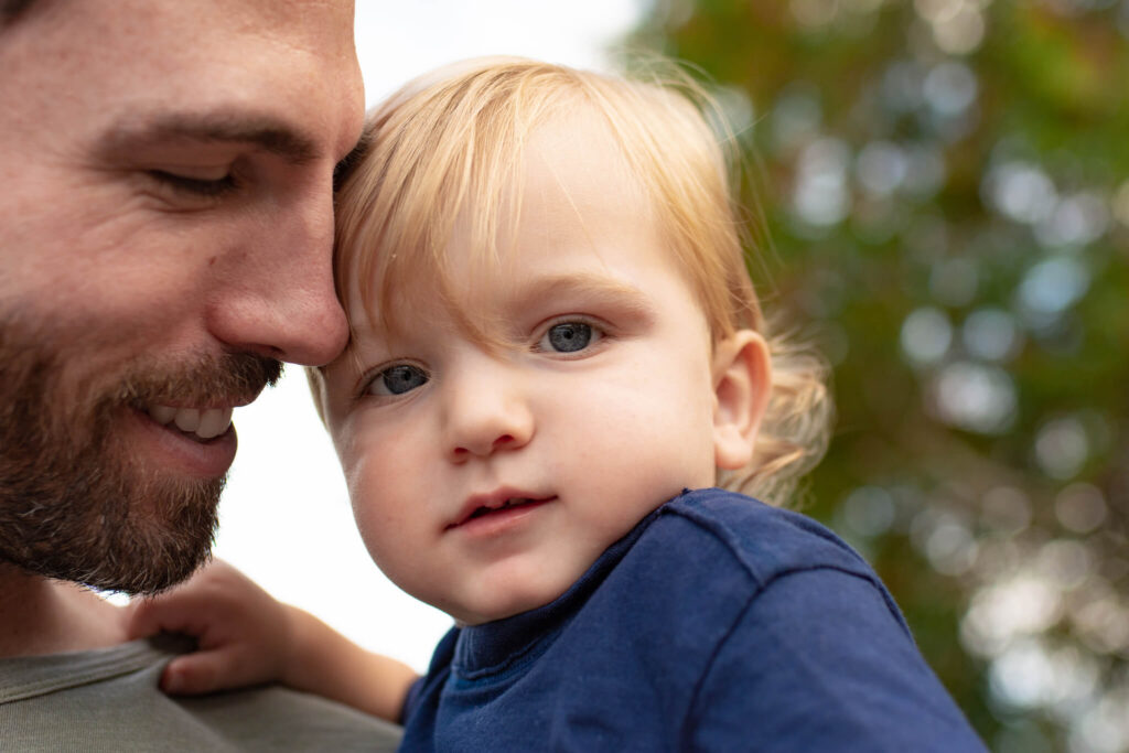 Father holding his blond toddler close during an outdoor family session, photographed by a Castle Rock family photographer as a meaningful Father’s Day photo gift.