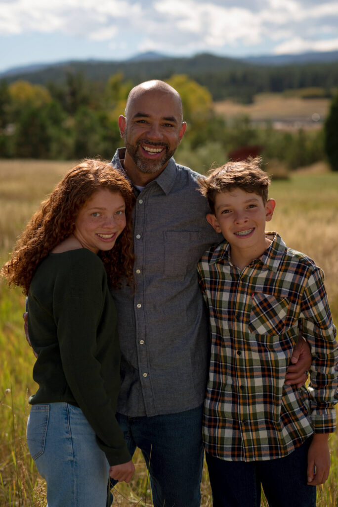 Father standing with his teenage son and daughter in an open Colorado field during a relaxed outdoor family photography session