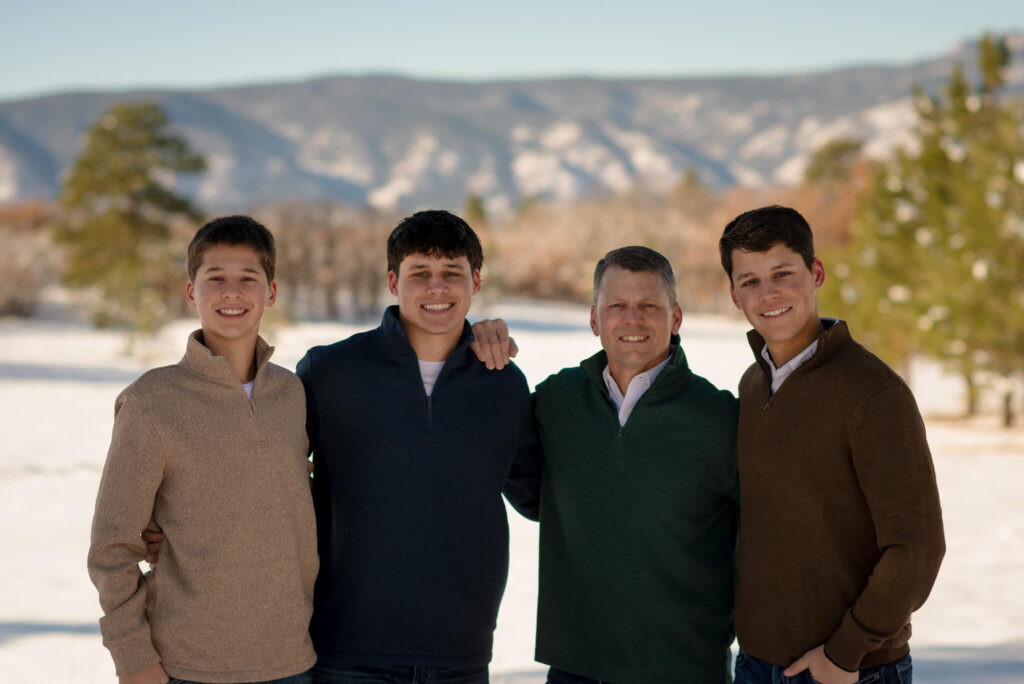 Dad posing with his three teenage sons in a snowy Colorado mountain setting during a winter family portrait session.