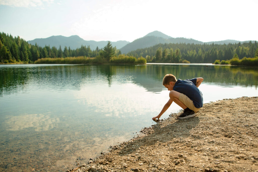 Young boy exploring the shoreline of a mountain lake during a summer family photo session in Colorado.