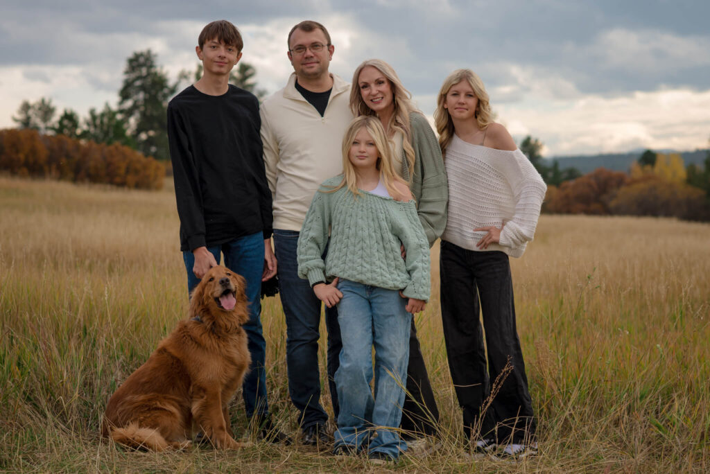 Family standing in a grassy meadow with their golden retriever during an outdoor family photo session in Colorado.