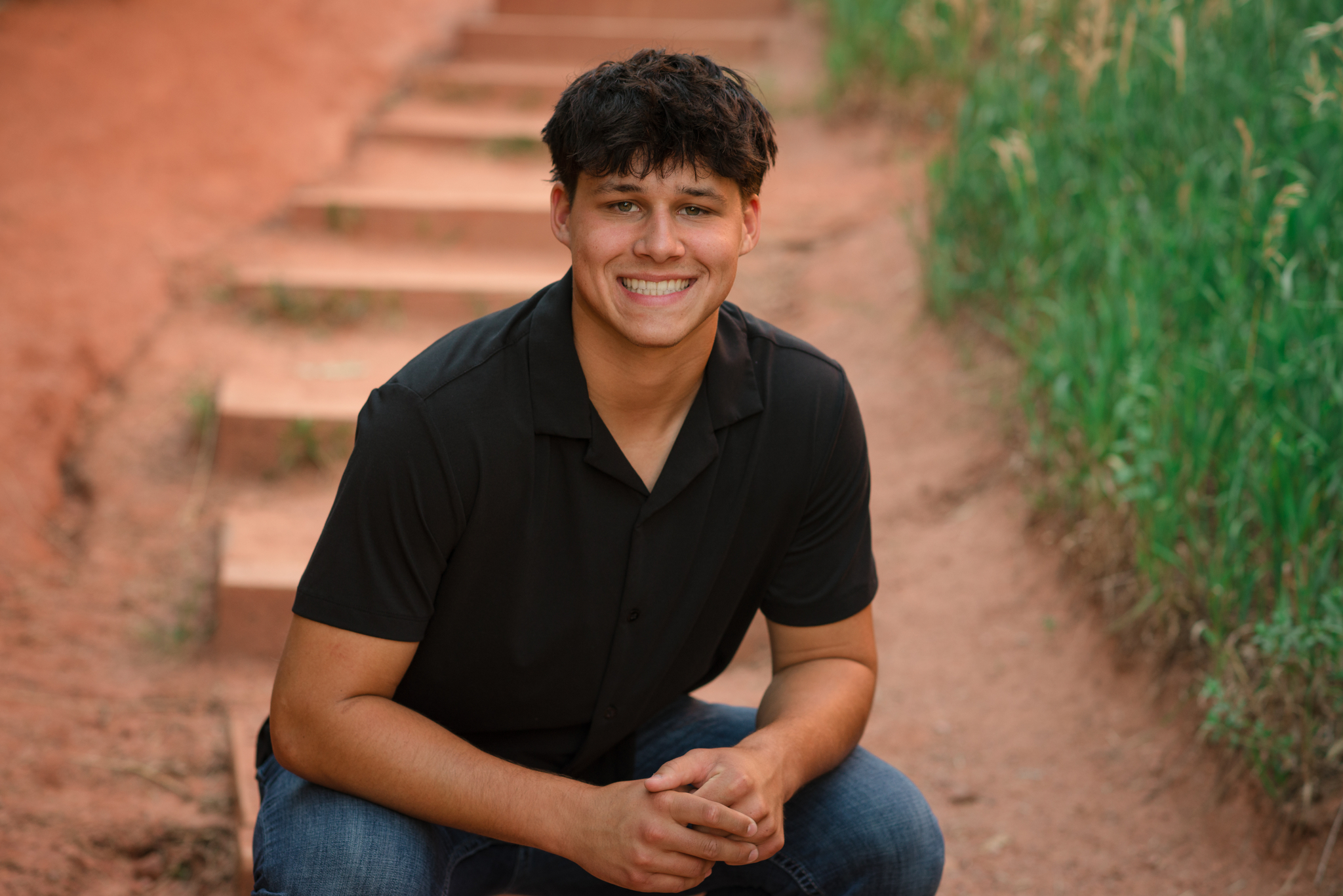 Colorado senior pictures for guys featuring a senior boy in a black shirt sitting near red rock formations.