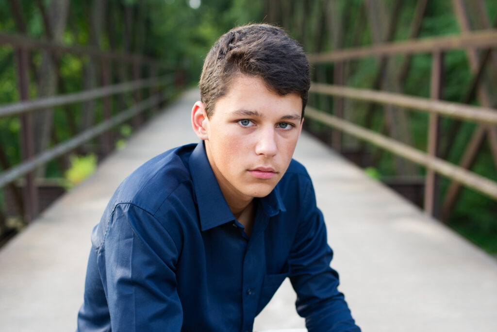 Colorado senior pictures for guys featuring a senior boy in a blue shirt posing on a wooded bridge.