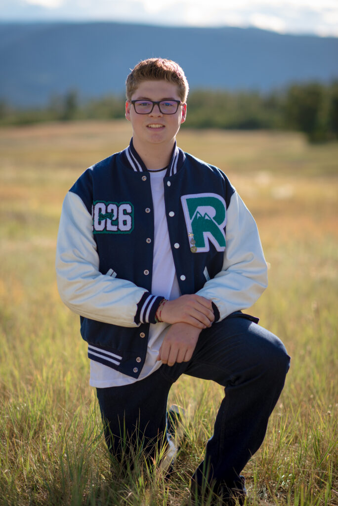 Colorado senior pictures for guys featuring a high school senior wearing his letterman jacket in an open field.