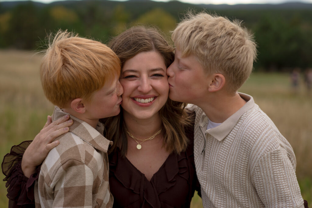 Castle Rock fall family mini session with a smiling mom as her two sons kiss her cheeks during an outdoor family photo session in Colorado.