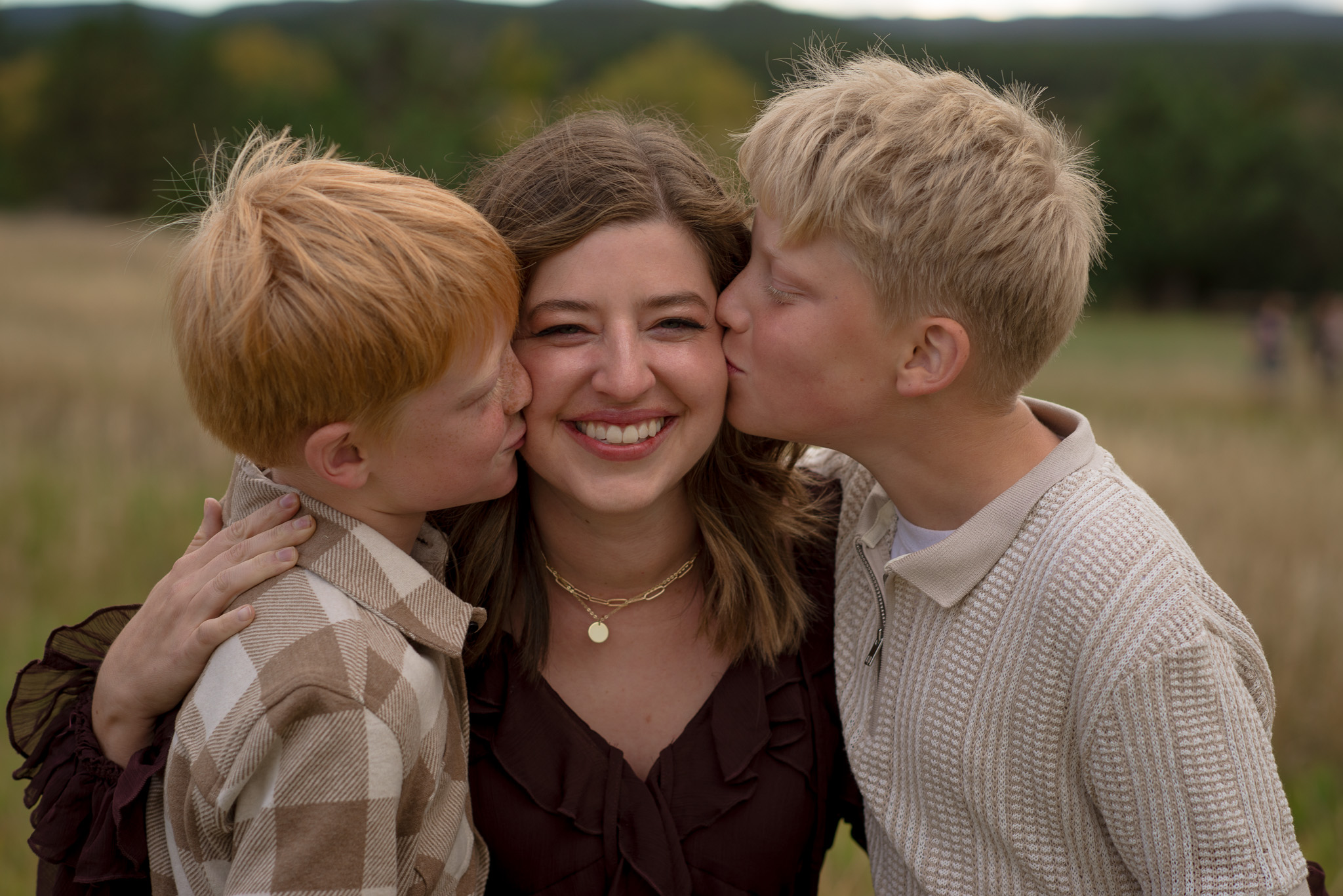 Castle Rock fall family mini session with a smiling mom as her two sons kiss her cheeks during an outdoor family photo session in Colorado.