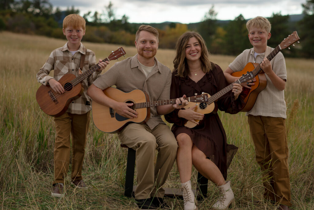Family of four holding guitars and ukuleles during a fall family mini session in Castle Rock, Colorado, surrounded by golden grasses and beautiful Colorado open space.
