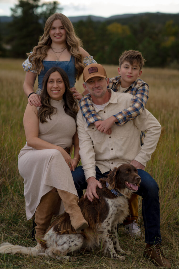 Family of four smiling together in a golden meadow during a fall family mini session in Castle Rock, Colorado.