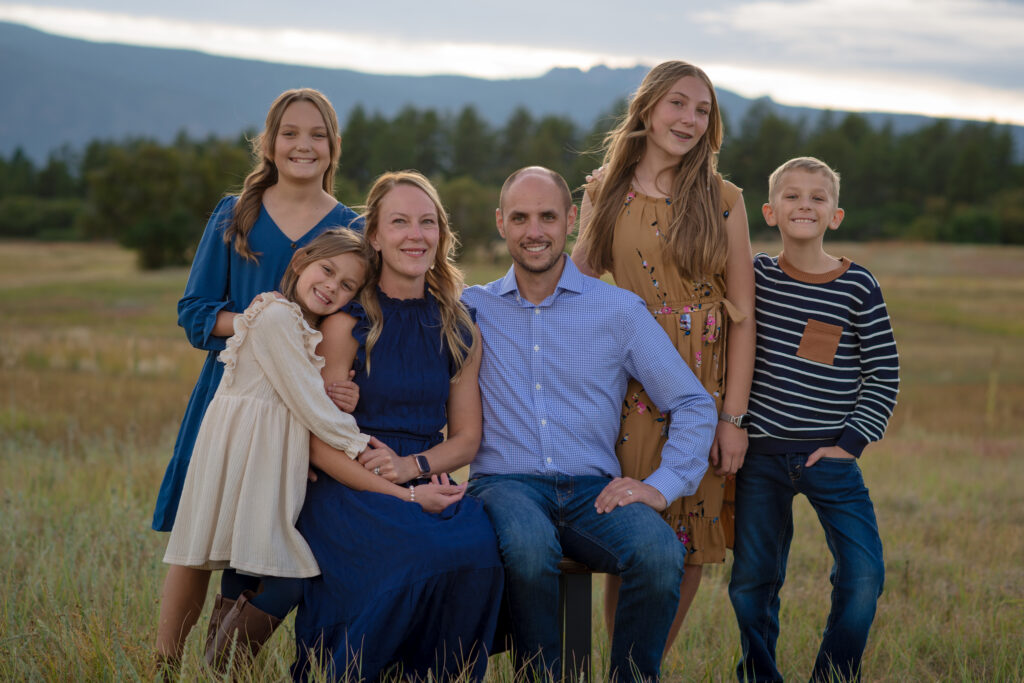 Family of six smiling together in a golden Colorado meadow with mountain views during a fall family mini session in Castle Rock, Colorado.
