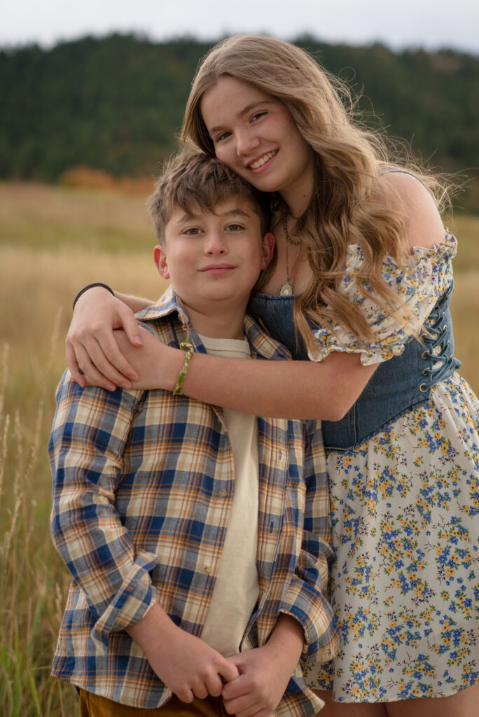 Brother and sister hugging and smiling in a Colorado meadow during a fall family mini session in Castle Rock, Colorado.