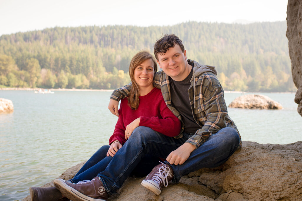 Mom and teenage son are sitting on a rock at Rattlesnake Lake.  Teenage son has his arm around his mother.