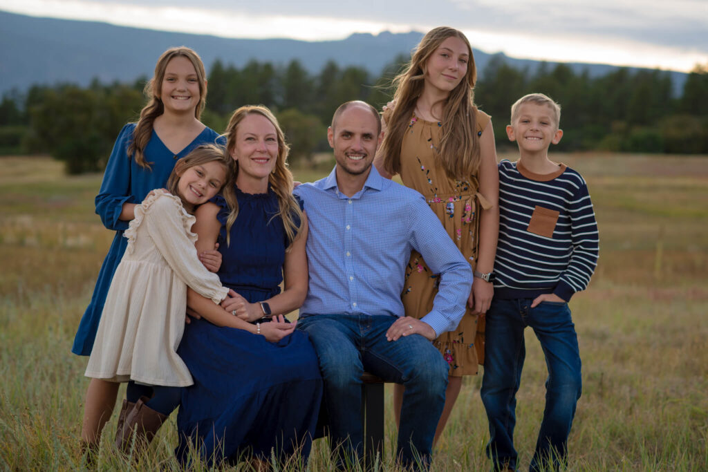 A family standing together in a sunlit Colorado field with fall foliage and mountains behind them, captured during a Colorado Family Photography session.