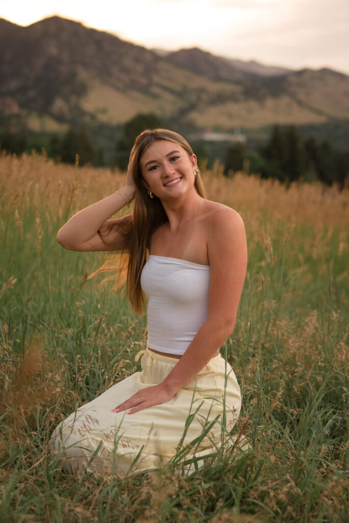 High school senior smiling during an outdoor Boulder senior photos session in a grassy field with mountain views at golden hour.
