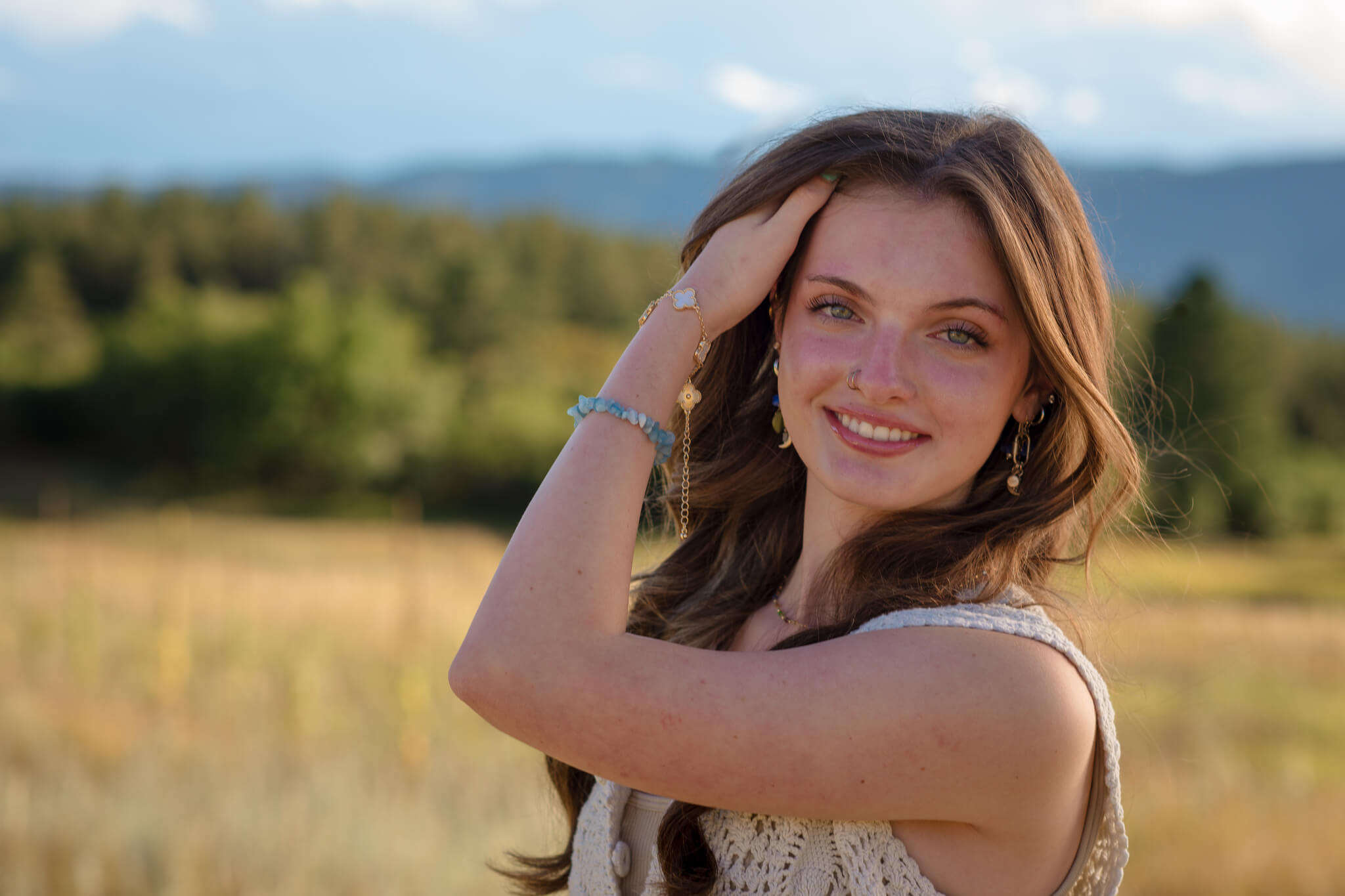 High school senior smiling during an outdoor photo session in Colorado with mountains in the background, photographed by a Castle Rock Senior photographer.
