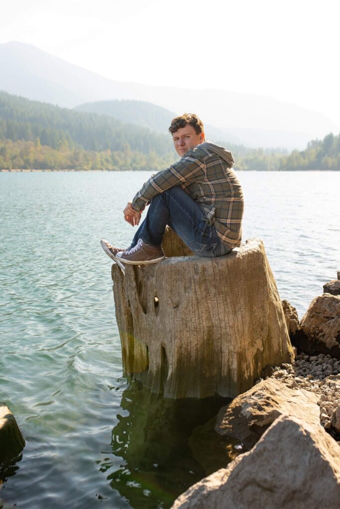 High school senior sitting on a rock by a mountain lake during an outdoor Castle Rock senior photos session.